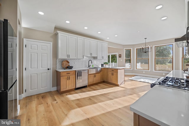 kitchen with appliances with stainless steel finishes, a peninsula, light wood finished floors, a sink, and light countertops