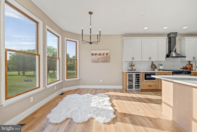 kitchen with wine cooler, wall chimney exhaust hood, decorative backsplash, a chandelier, and pendant lighting