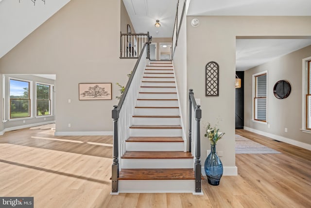 staircase featuring baseboards, wood finished floors, attic access, and a towering ceiling