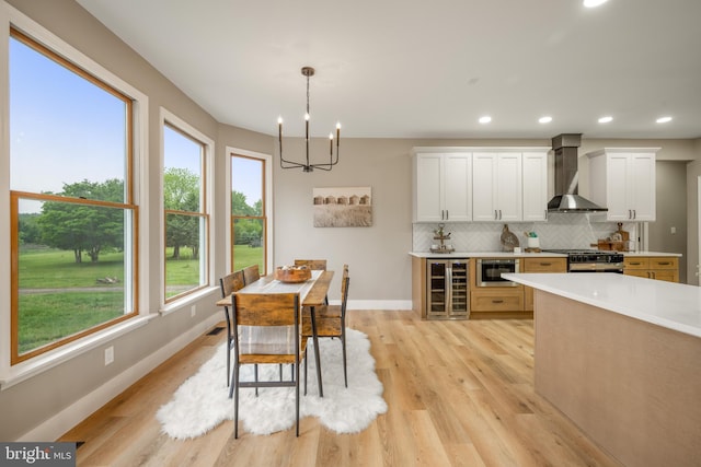 kitchen featuring wall chimney range hood, wine cooler, a chandelier, stainless steel range with gas stovetop, and backsplash