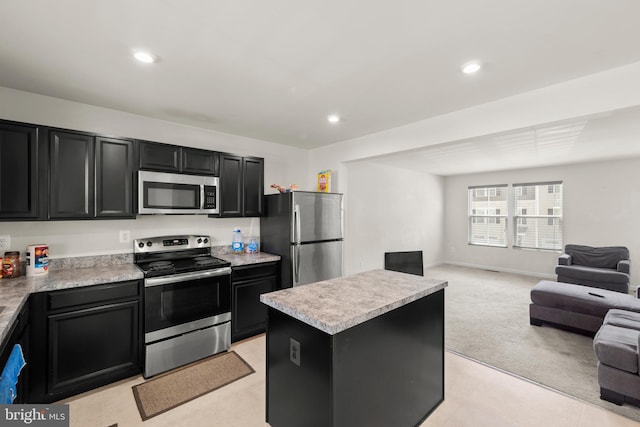 kitchen with appliances with stainless steel finishes, dark cabinetry, open floor plan, light countertops, and a center island
