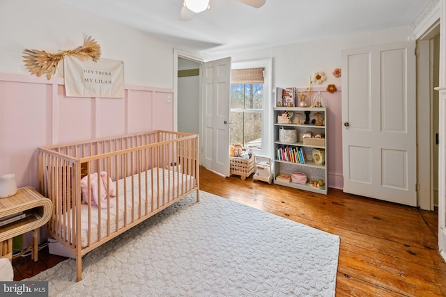 3947 Hebron Valley Rd, Madison, VA 22727 - bedroom with wood-type flooring, a crib, wainscoting, and a ceiling fan
