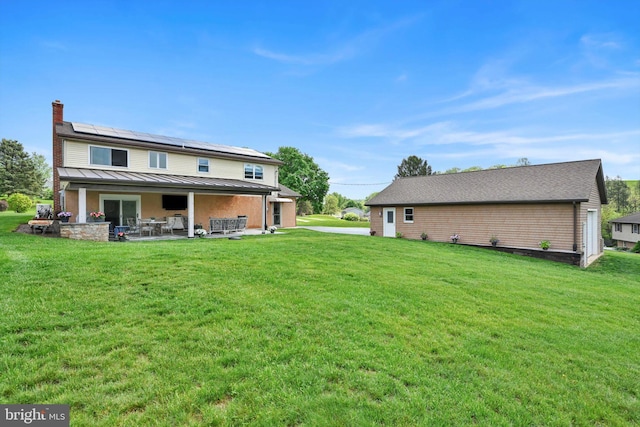 191 Meadow Dr, Mohrsville, PA 19541 - back of house with a chimney, roof mounted solar panels, a patio, a standing seam roof, and a lawn