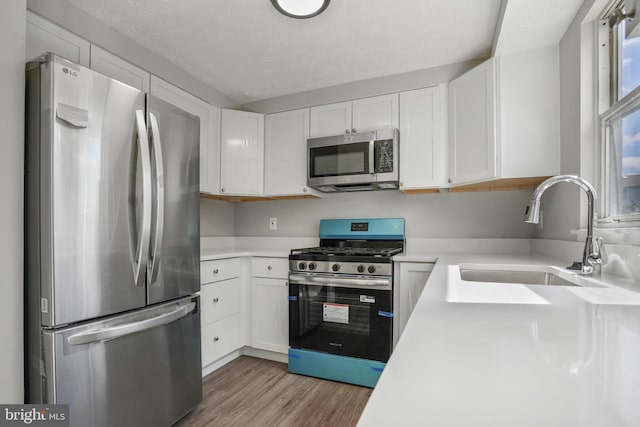 kitchen with stainless steel appliances, a sink, light wood-style flooring, light countertops, and white cabinets