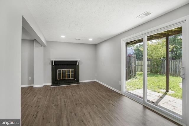unfurnished living room with dark wood-type flooring, a textured ceiling, baseboards, a glass covered fireplace, and recessed lighting