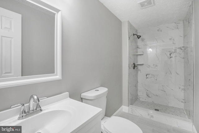 bathroom featuring toilet, a marble finish shower, a textured ceiling, vanity, and baseboards