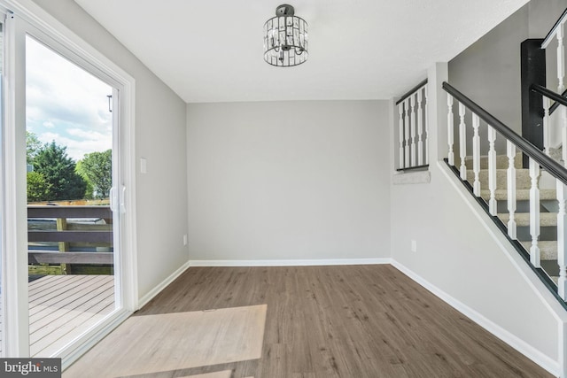 unfurnished dining area featuring wood finished floors, a chandelier, baseboards, and stairs