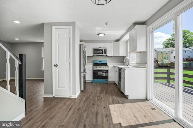 kitchen featuring stainless steel appliances, a sink, dark wood-type flooring, white cabinetry, and light countertops