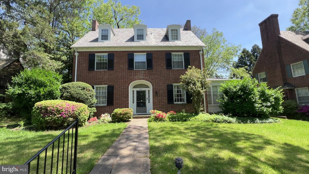 colonial inspired home with brick siding, a front lawn, and a chimney