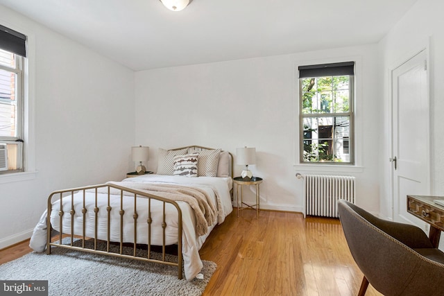 bedroom with radiator, wood finished floors, and baseboards