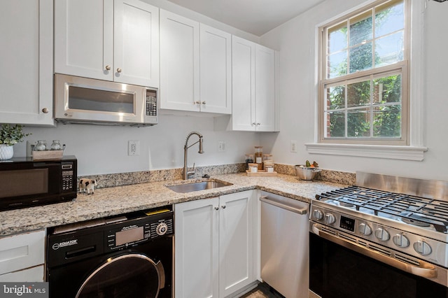 kitchen featuring washer / dryer, stainless steel appliances, a sink, white cabinetry, and light stone counters