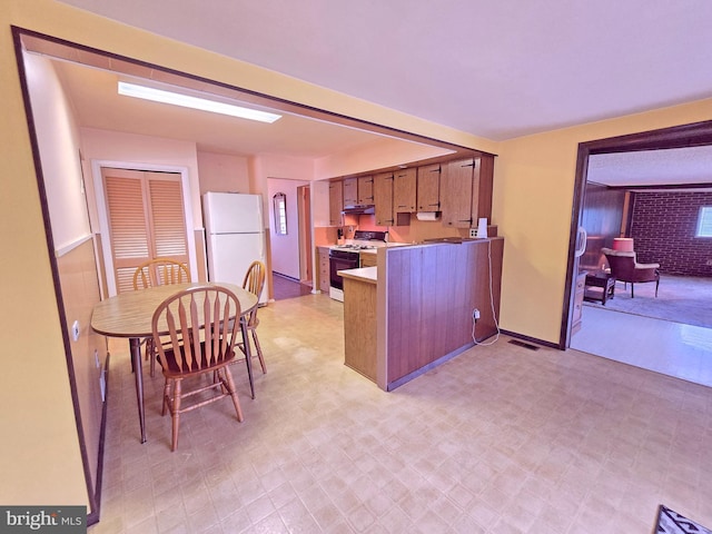 kitchen featuring white appliances, a peninsula, under cabinet range hood, and light flooring