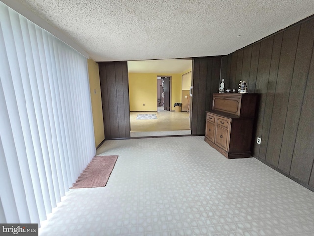 unfurnished bedroom with wooden walls, light colored carpet, and a textured ceiling