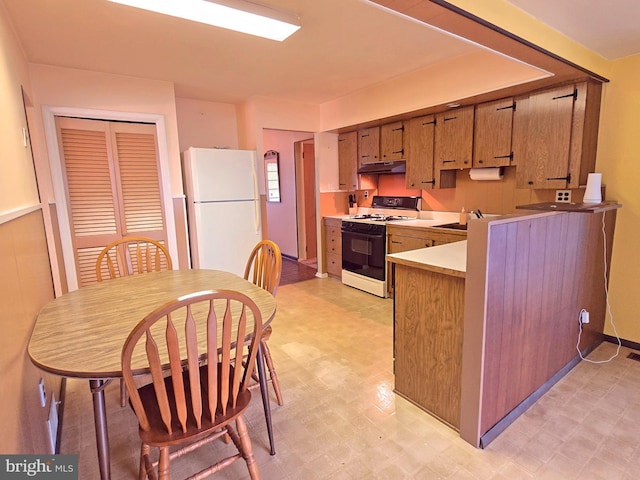kitchen with range with gas stovetop, freestanding refrigerator, light floors, under cabinet range hood, and light countertops