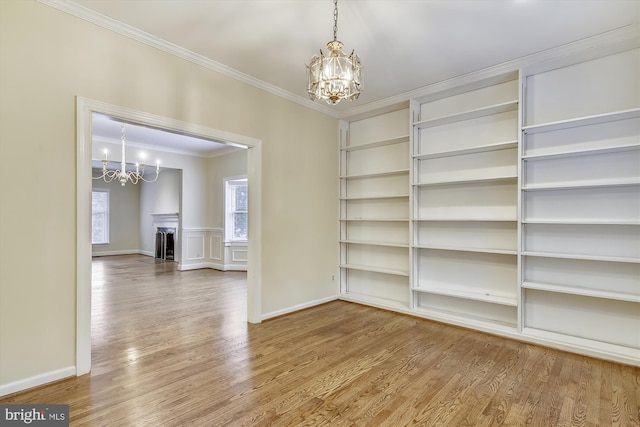 empty room with a chandelier, crown molding, wood finished floors, built in features, and a fireplace