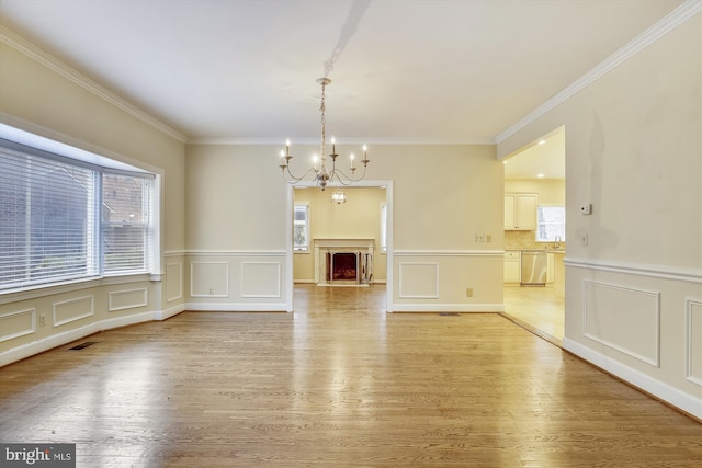 unfurnished dining area featuring a chandelier, a decorative wall, ornamental molding, light wood-style floors, and wainscoting