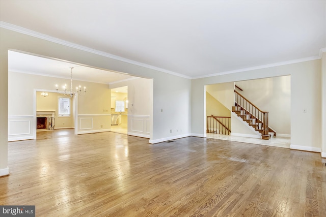 unfurnished living room featuring light wood-type flooring, stairs, crown molding, a chandelier, and a fireplace