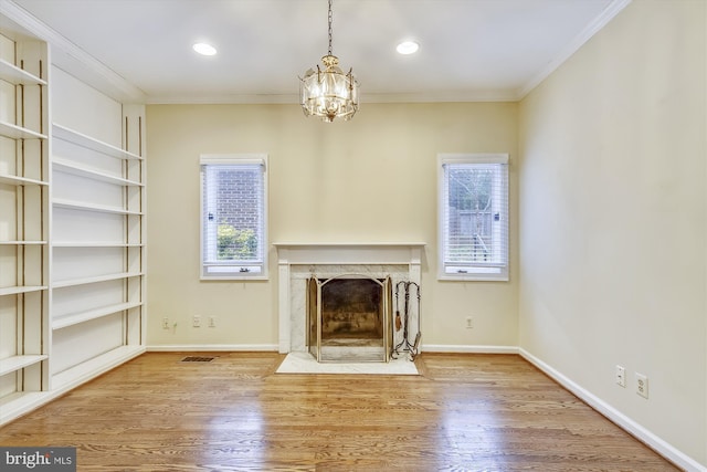 unfurnished living room featuring a premium fireplace, ornamental molding, a chandelier, wood finished floors, and baseboards