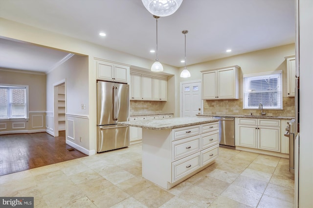 kitchen with stainless steel appliances, crown molding, a sink, a center island, and light stone countertops