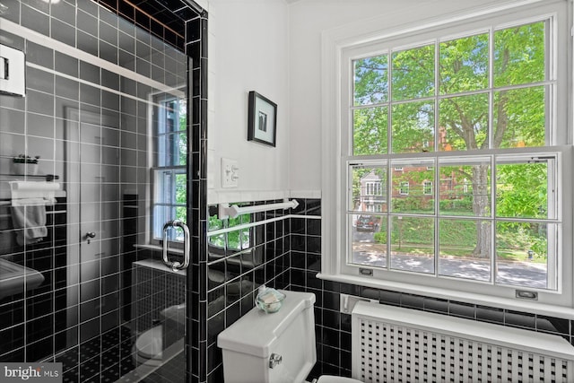 bathroom with radiator heating unit, tile walls, a shower stall, and toilet