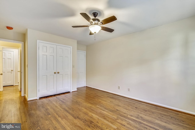 unfurnished bedroom featuring wood finished floors, baseboards, a closet, and a ceiling fan