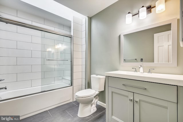 bathroom with toilet, vanity, bath / shower combo with glass door, and baseboards