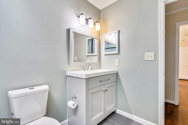 half bathroom with toilet, baseboards, vanity, and ornamental molding