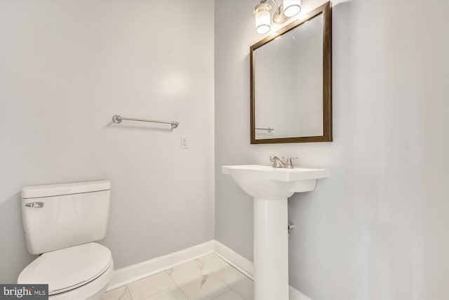 half bath featuring baseboards, marble finish flooring, and toilet