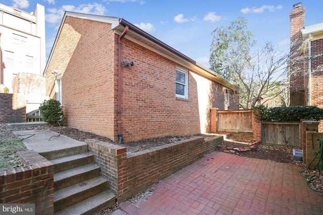 view of home's exterior with a patio, brick siding, and fence