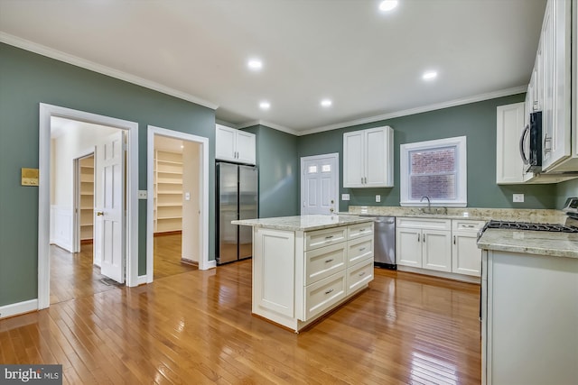 kitchen with appliances with stainless steel finishes, crown molding, a kitchen island, a sink, and white cabinets