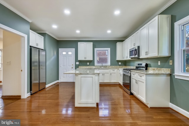 kitchen featuring appliances with stainless steel finishes, a sink, ornamental molding, a kitchen island, and white cabinets