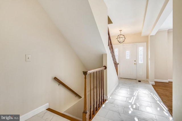 foyer entrance with marble look tiles, baseboards, and a chandelier