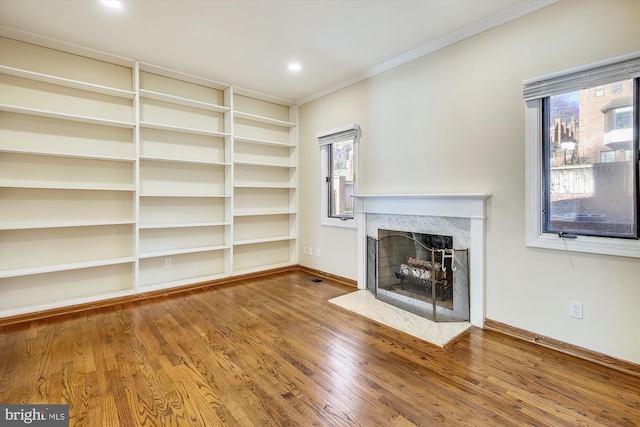 unfurnished living room featuring ornamental molding, a premium fireplace, healthy amount of natural light, wood finished floors, and baseboards