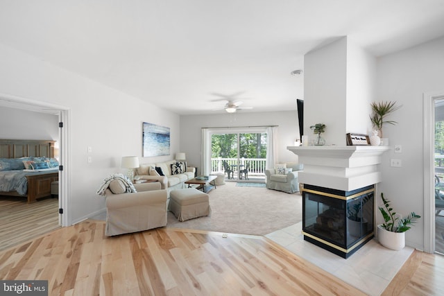 living area featuring a ceiling fan, wood finished floors, a multi sided fireplace, and baseboards