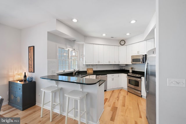 kitchen featuring appliances with stainless steel finishes, a peninsula, light wood finished floors, white cabinets, and recessed lighting
