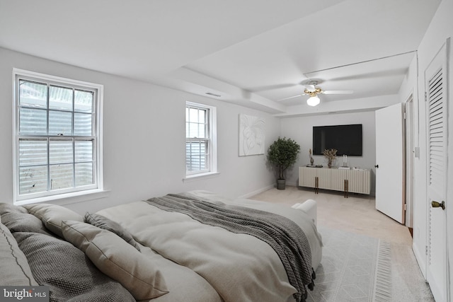 bedroom featuring light carpet, ceiling fan, and a tray ceiling