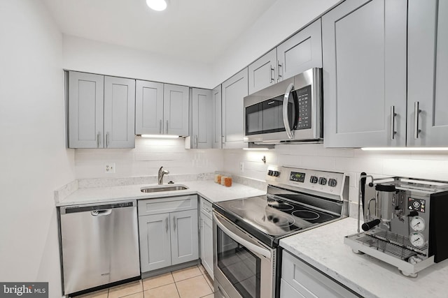kitchen with appliances with stainless steel finishes, gray cabinets, a sink, and tasteful backsplash