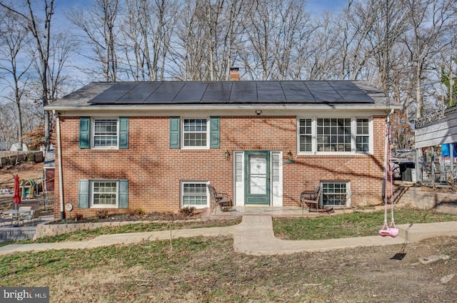 split foyer home featuring a chimney, solar panels, and brick siding