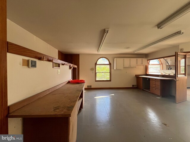 8107 Chester St, Takoma Park, MD 20912 - kitchen featuring concrete flooring, a peninsula, healthy amount of natural light, and white cabinetry