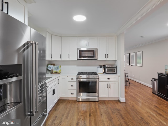kitchen with appliances with stainless steel finishes, light countertops, ornamental molding, white cabinets, and dark wood-type flooring
