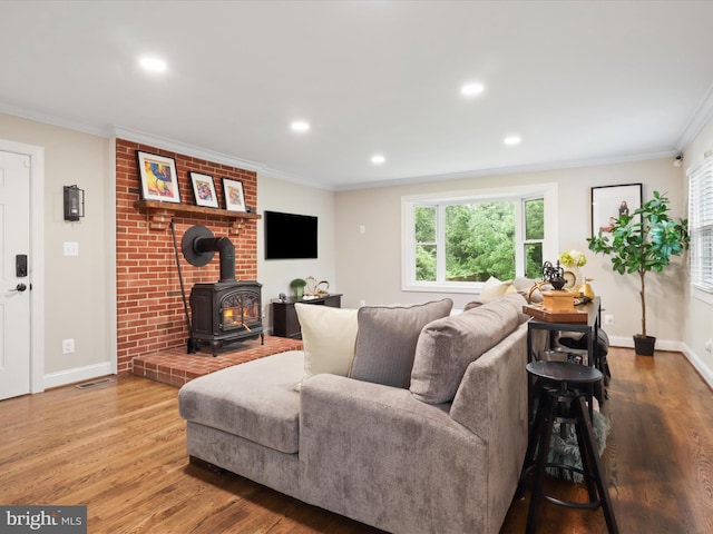 living area featuring a wood stove, wood finished floors, crown molding, baseboards, and recessed lighting