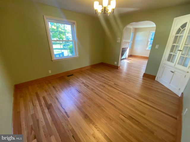 unfurnished dining area with arched walkways, light wood-style floors, a chandelier, and baseboards
