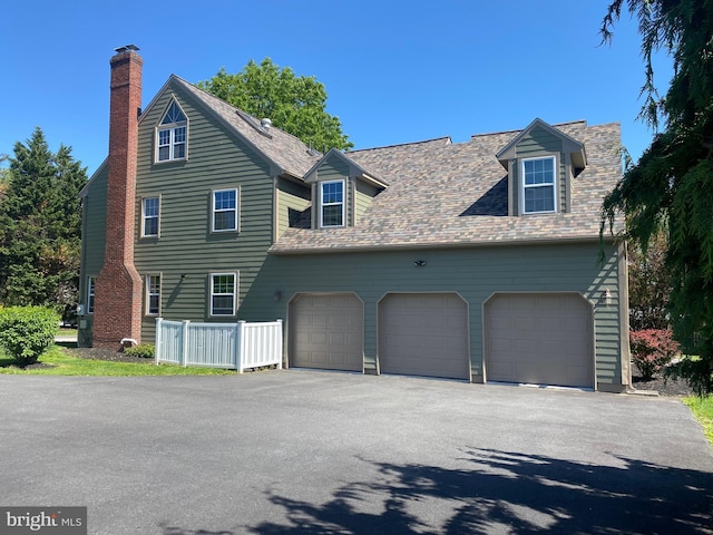 view of front of property featuring asphalt driveway, an attached garage, a chimney, fence, and roof with shingles