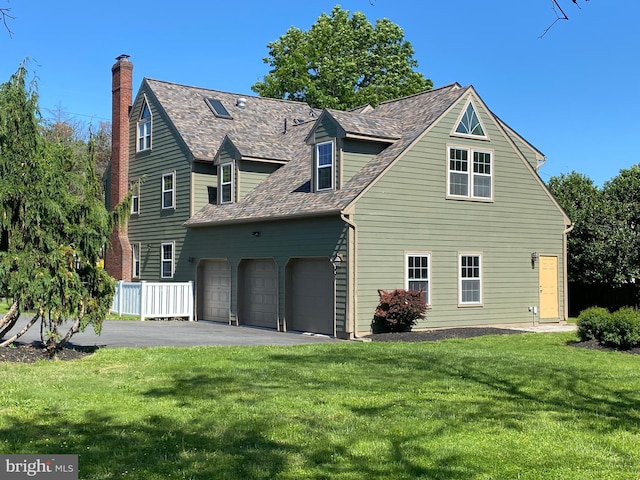 view of side of home featuring a chimney, a garage, a yard, asphalt driveway, and roof with shingles