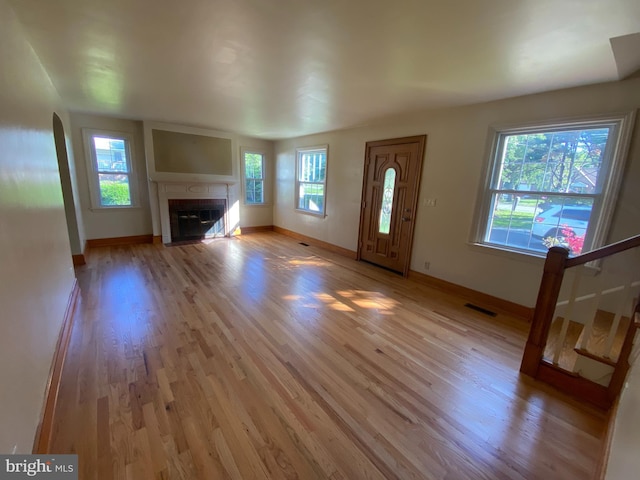 unfurnished living room with light wood-style flooring, a fireplace with flush hearth, and baseboards