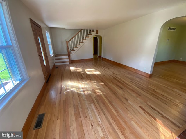 unfurnished living room with arched walkways, light wood finished floors, stairs, and baseboards