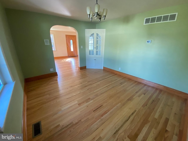 unfurnished dining area featuring arched walkways, a chandelier, light wood finished floors, and baseboards