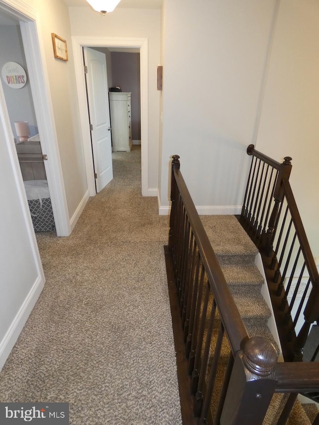 hall featuring carpet flooring, baseboards, and an upstairs landing