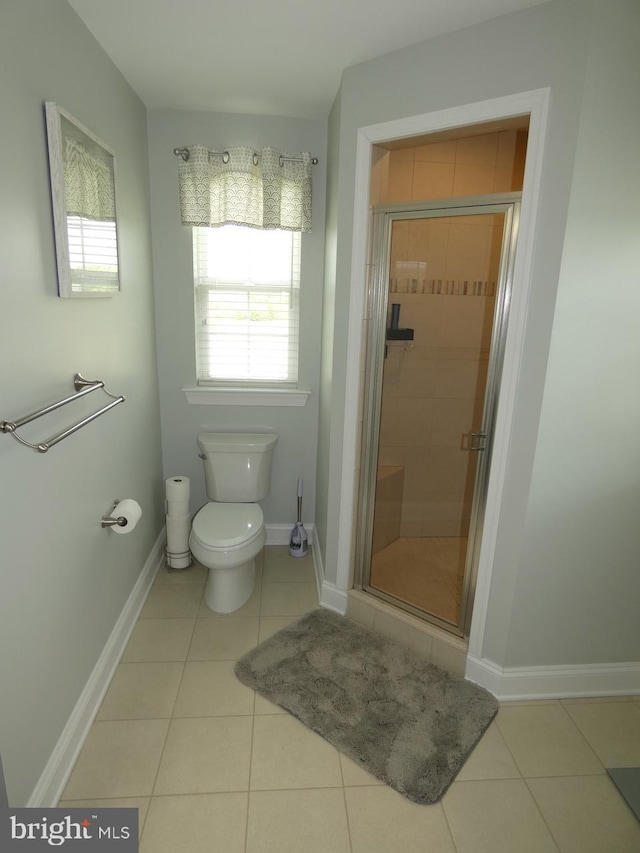 bathroom featuring toilet, tile patterned flooring, a stall shower, and baseboards