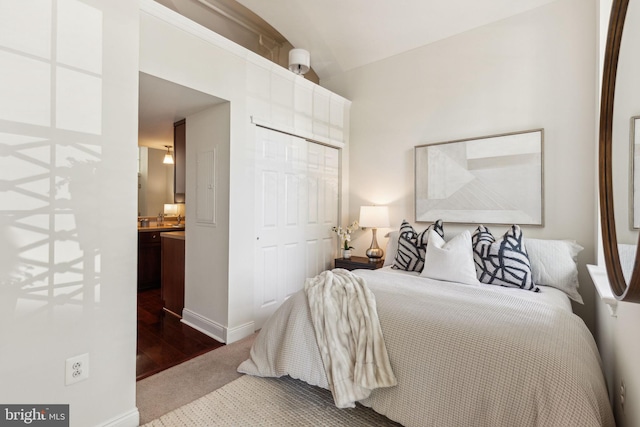 bedroom featuring dark carpet, a closet, vaulted ceiling, connected bathroom, and baseboards